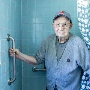 Old man holding a vertical grab bar in shower